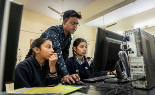 An educator helps two young people at a computer.