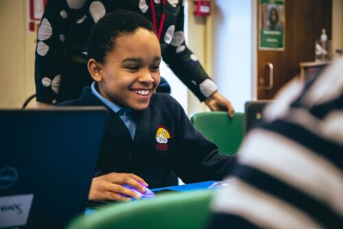 A young person smiles while using a laptop.