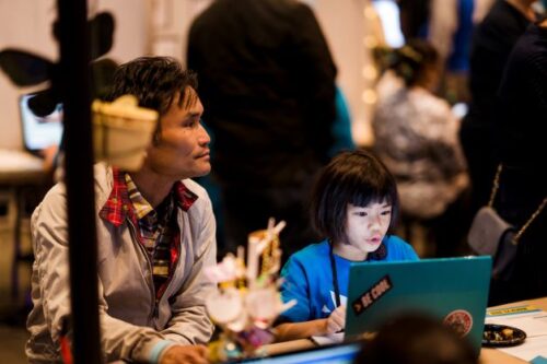 A young person creating a project at a laptop. An adult is sat next to them.