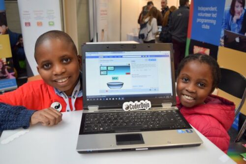 Two young people share their Scratch project on a laptop.