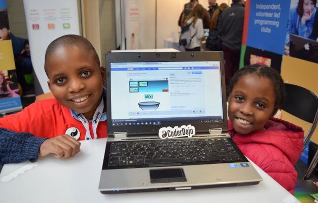 Two young people share their Scratch project on a laptop.