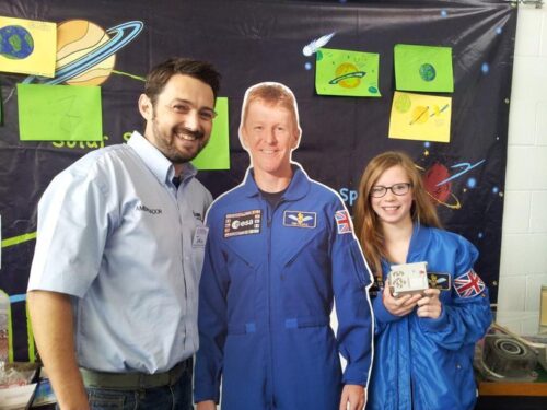 A young person and adult pose with a cardboard astronaut Tim Peake and an Astro Pi computer.