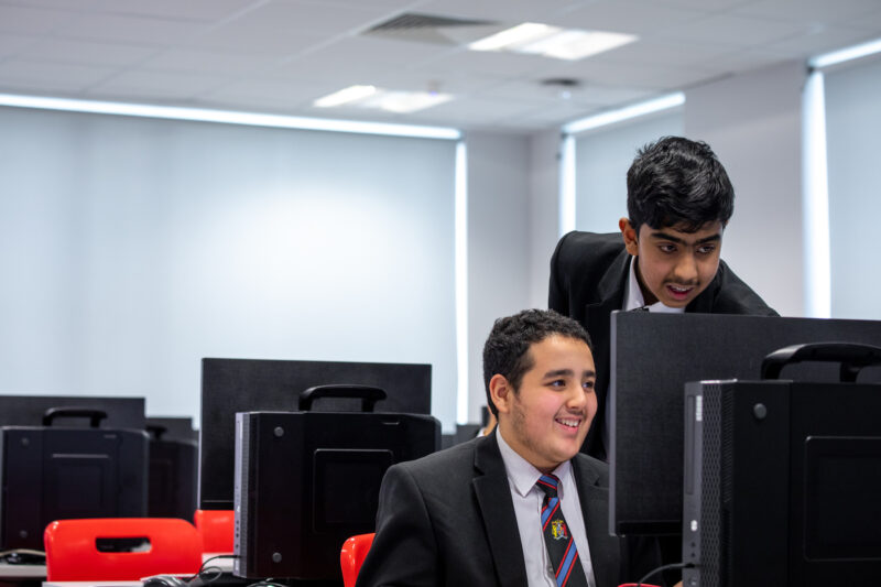 Two smiling computer science students at a desktop computer in a classroom.