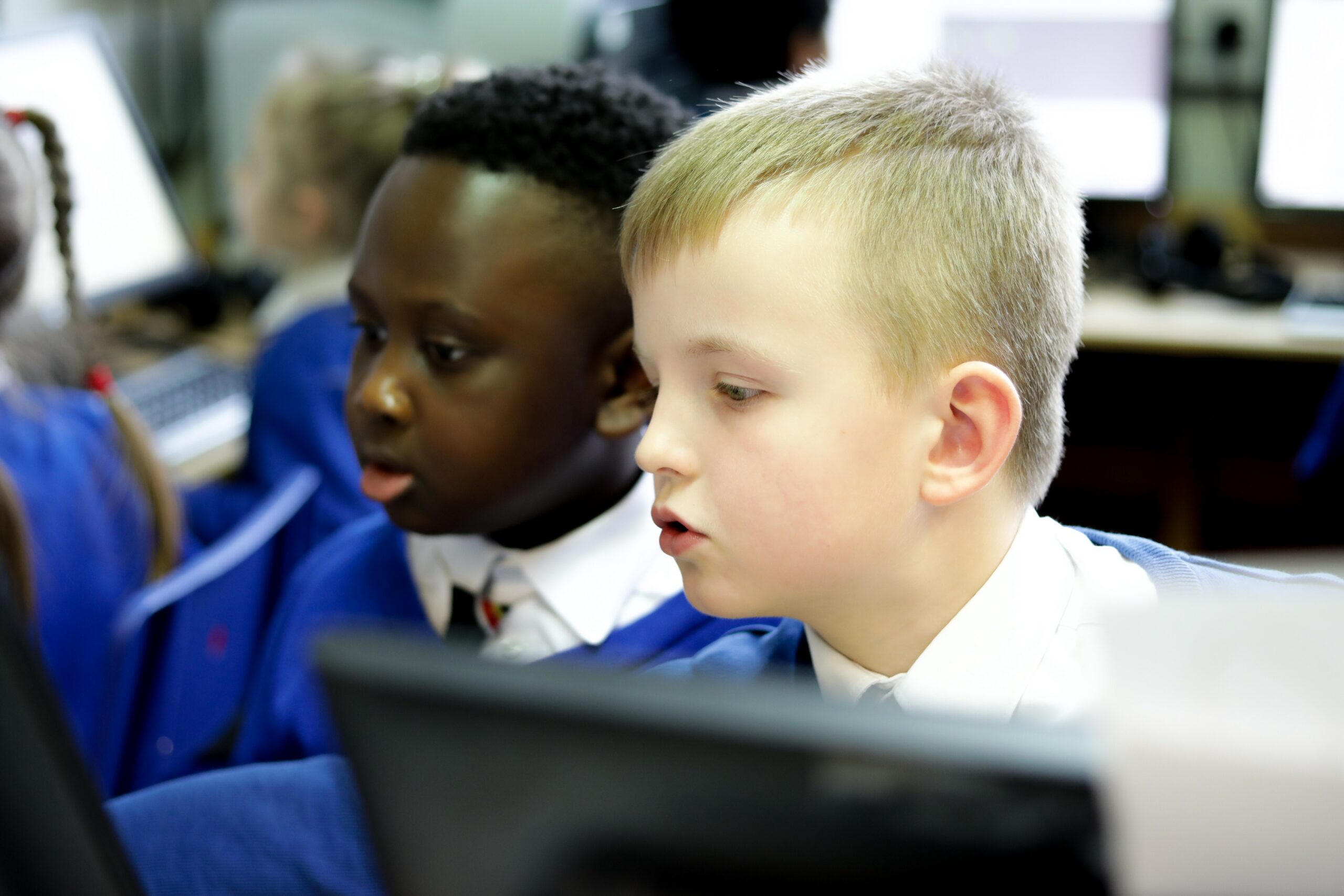 In a computing classroom, two young children look at a computer screen.