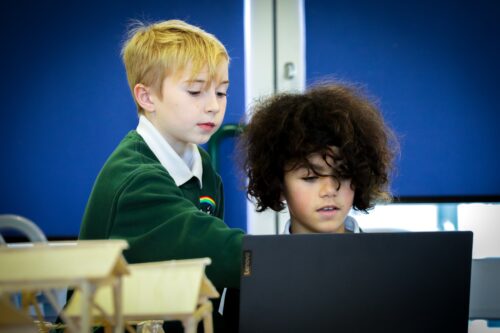 Two learners at a laptop in a computing classroom.