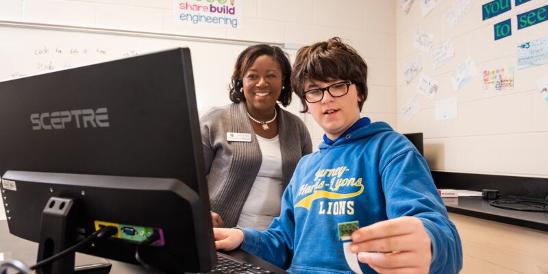 A teacher assisting a young person with a coding project.