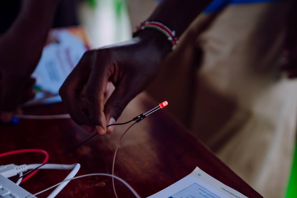 A close-up shot shows a person's hand holding a small red LED light, which is illuminated. 
