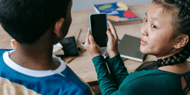 Photo of a young person showing their mobile phone to a peer.
