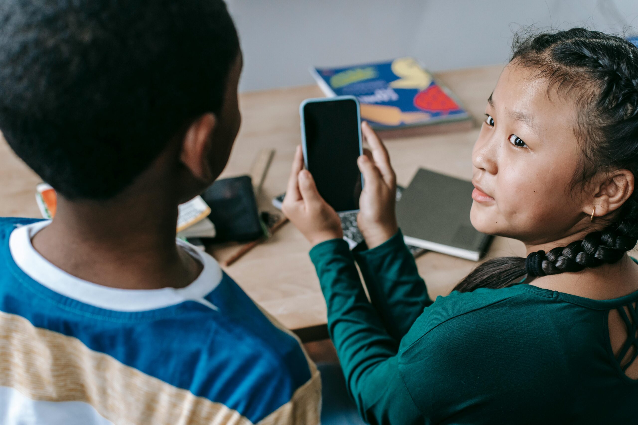 Photo of a young person showing their mobile phone to a peer.
