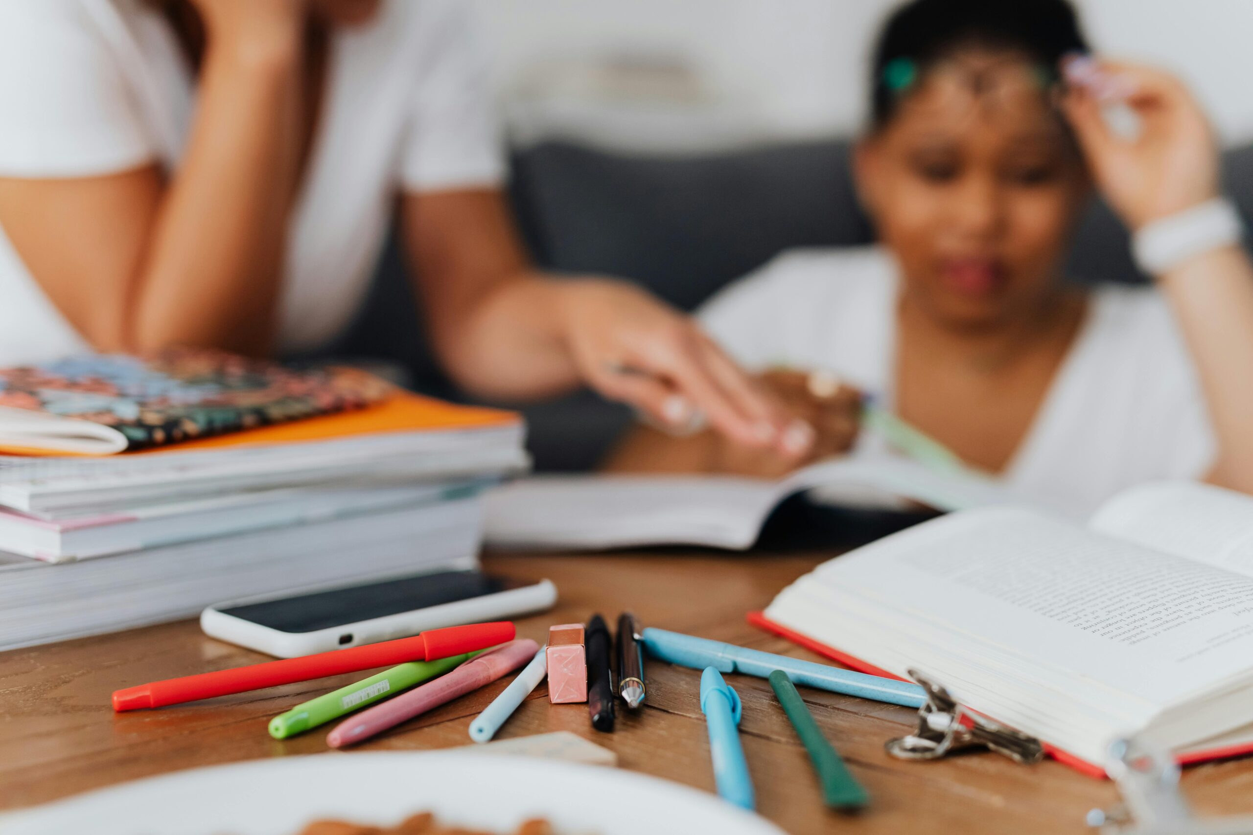 Close up photo of a desk with school books, various coloured pens and a mobile phone in shot.