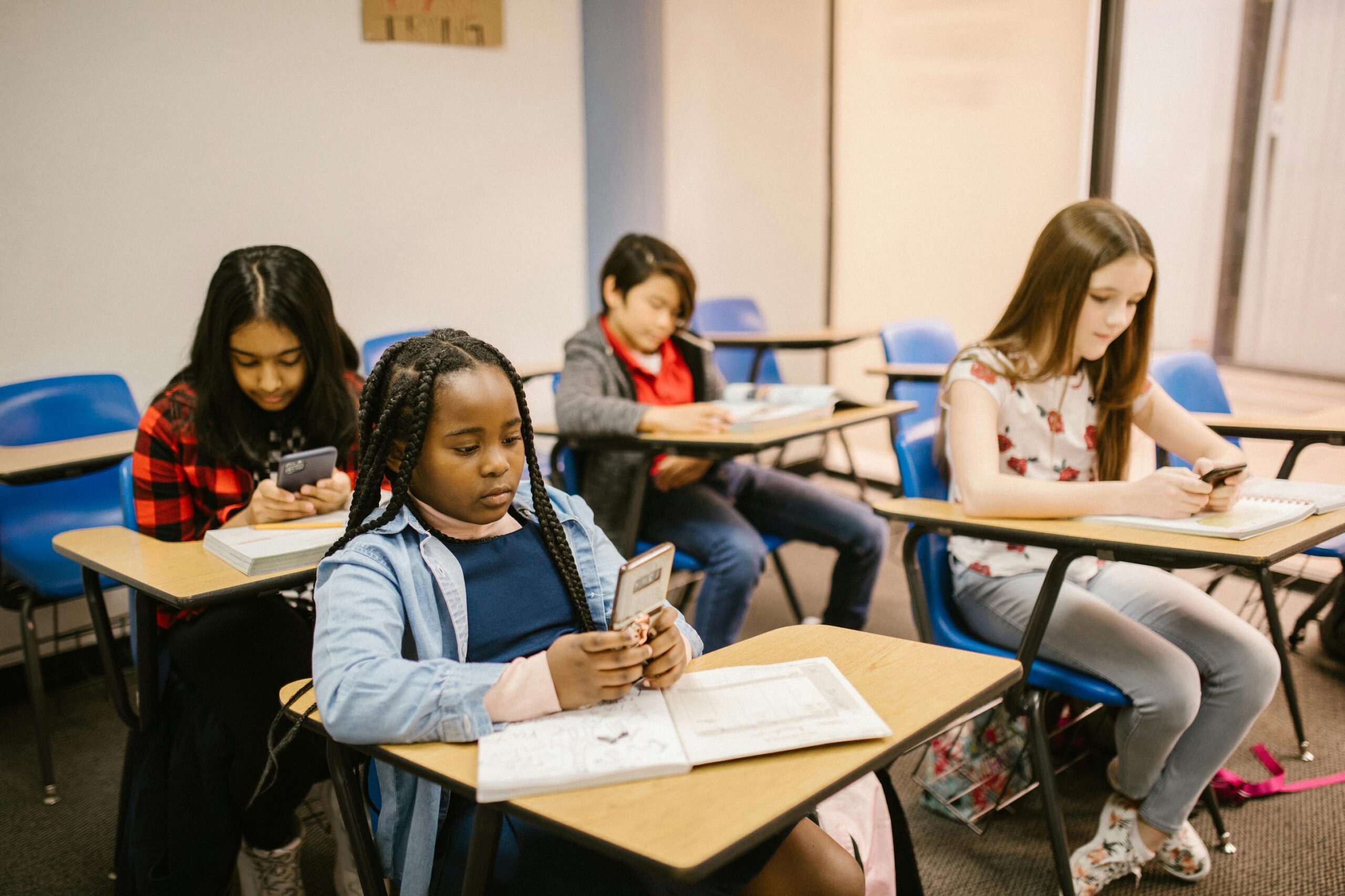 Photo of four young people sitting at their desks, on their mobile phones.