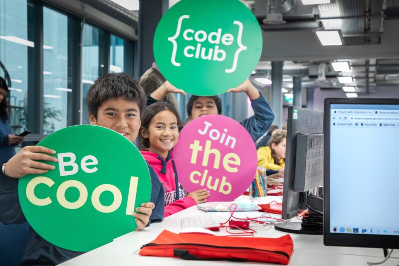 Three young persons cheer at a Code Club.