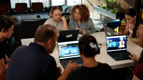 Photo of two adult educators sitting around a table with a group of young people playing AI Quests.