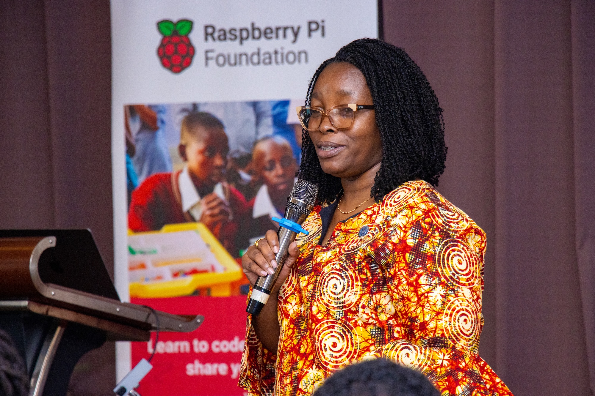 A speaker at the Raspberry Pi Foundation's Kenya Partner Showcase 2025, smiling and holding a microphone.