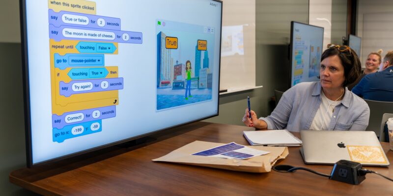 A teacher explores an Experience CS Scratch project on a large screen.