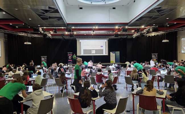 Young people coding Mission Zero at tables in a large events space.