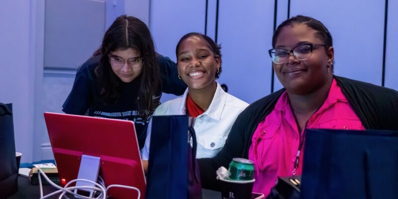 Three smiling young tech creators at a computer screen during a Code Club session in Aruba.