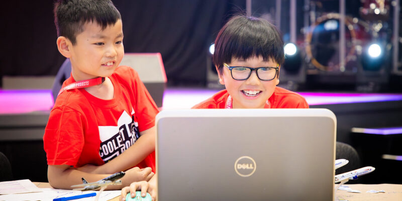 Two young tech creators smile at a laptop at a Coolest Projects event.