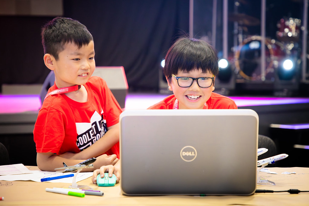 Two young tech creators smile at a laptop at a Coolest Projects event.