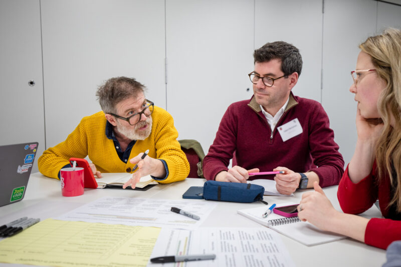 Teachers sit at a table discussing England's curriculum review and The Future of England's Computing Curriculum.