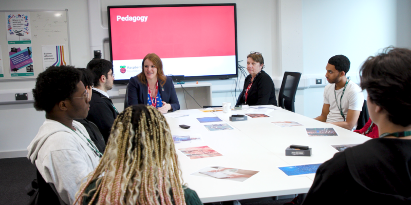 Students and educators sit at a table discussing The Future of England's Computing Curriculum.