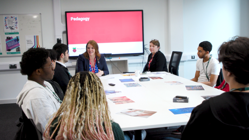 Students and educators sit at a table discussing England's curriculum review and The Future of England's Computing Curriculum.