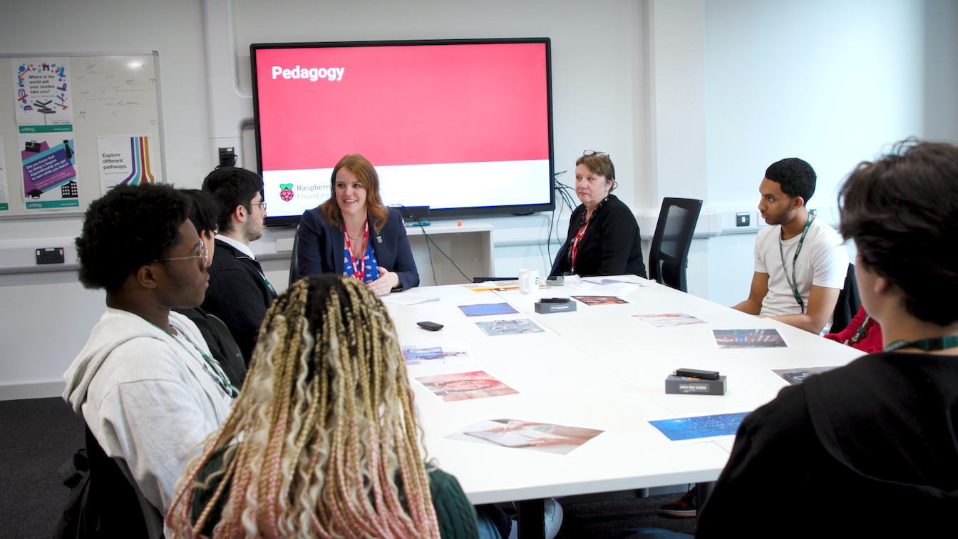 Students and educators sit at a table discussing The Future of England's Computing Curriculum.