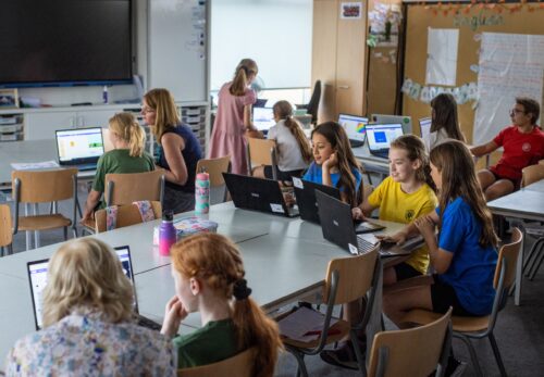 A Code Club session in a school classroom filled with young people working together at laptops.