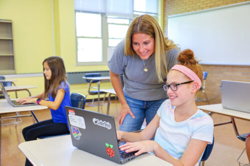 A young person and a teacher looking at a laptop in a classroom setting.