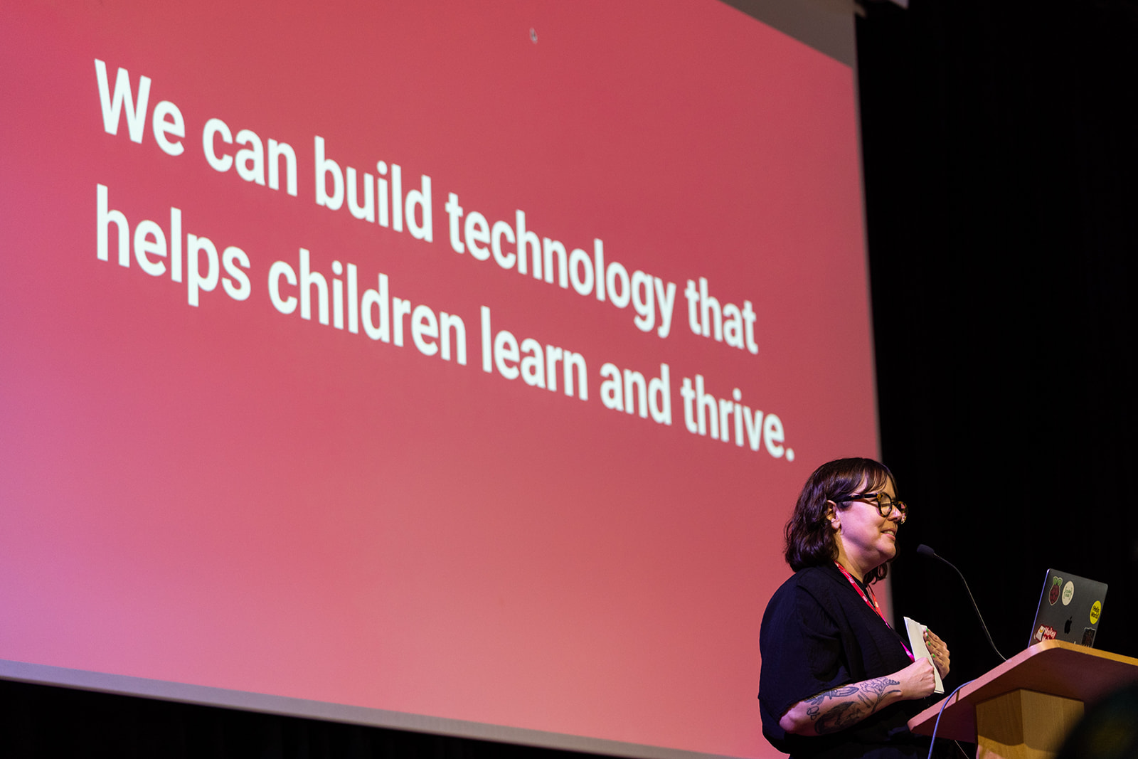 A person on stage stands before a slide with the sentence "We can build technology that helps children learn and thrive".